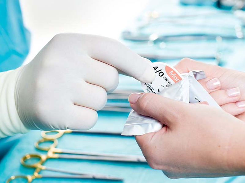 Hand with glove removes suture material from a sterile package